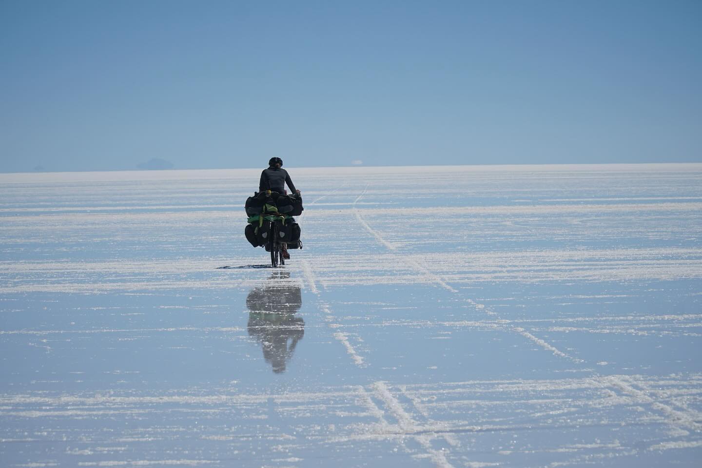 Die drei Tage ohne Fahrrad taten gut, doch wir freuten uns auch wieder weiter fahren zu können. Vorallem stand eines der absouluten Highlights an. Mit den Rädern auf den Salzsee. 1 ½ Tage nichts außer weiß. Keine Straßen, keine Menschenseele, nur wir mit unseren Fahrrädern. Man fährt km um km und man verliert jegliche Orientierung. Der Süden sieht genauso aus wie der Norden oder der Westen oder der Osten. Nur eine kleine Orientierung am Horizont und die Sonne. Der Vulkan Tunupa der aber am Fuß auch über 15 km Breite hat. Ohne Navi hätten wir den Ausgang also auch so nicht gefunden. Ein nichts aus weiß und trotzdem unbeschreiblich schön. Doch das Fahren an sich war mühsam. Da die Regenzeit gerade erst zu Ende gegangen ist, war das Salz noch sehr nass und es fühlte sich so an, als würde man über Kleber fahren. Dazu hatte man das Gefühl gar nicht vom Fleck kommt. Am Nachmittag hielten wir deshalb einfach an und schlugen mitten auf der weißen Ebene unser Zelt auf. Genossen noch den wunderschönene Sonnenuntergang und gingen relativ früh schlafen. Denn wir wollten uns unbedingt den Sternenhimmel anschauen. Die Erwartungen waren zwar schon hoch, doch was wir sahen übertraf alles, was man sich hätte vorstellen können. Ein Bild, das keine Kamera einfangen kann. Ein Bild das einfach nur unbeschreiblich ist.
Die restlichen 60 km legten wir dann am nächsten Vormittag auf dem Salar zurück. Zum Glück auch mit besseren Bodengegebenheiten, sodass wir nicht mehr nur noch das Gefühl hatten, am Boden zu kleben.
Doch der Salzsee hat auch Spuren hinterlassen. Nicht nur wir waren von oben bis unten voller Salz, auch unsere Taschen und Fahrräder waren komplett gesalzen. Das konnte natürlich unmöglich so bleiben, da dir Fahrräder sonst wahrscheinlich schon auf dem Weg nach La Paz völlig verrostet gewesen wären. Wir verbrachten also den ganzen Nachmittag damit, unsere Fahrräder in der Wasserquelle vom Vulkan (die einzige Wasserquelle, die nicht salzig war) sauber zu machen.