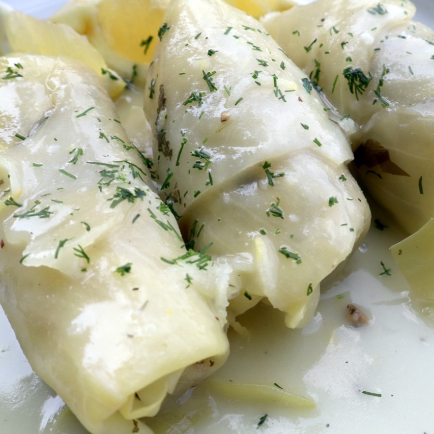 Lahanodolmades: Griechische Kohlrouladen wie bei Mama. Die Kohlrouladen: 1 Weißkohl, Salz, 500 g Rinderhackfleisch, 200 g Carolina-Reis, ½ TL Kreuzkümmel, 1 Zwiebel, 1 Knoblauchzehe, ⅓ Bund Dill, ⅓ Bund Minze, ⅓ Bund Petersilie
3 EL Rosmarin (gehackt), Pfeffer, 3–4 EL Olivenöl. Für die Sauce: 70 g Butter, 70 g Weizenmehl, 700 ml Wasser, 1 Hähnchen-Brühwürfel, Zitronenschale und -saft von 1–2 Bio-Zitronen, Pfeffer, 1 EL Olivenöl
Kohl vorbereiten:gGroßen Topf mit Salzwasser zum Kochen bringen, Strunk vom Kohls entfernen, mit der
Strunkseite nach unten ins kochende Wasser legen. Die äußeren Blätter mit einem Löffel nach und nach ablösen, sobald sie weich werden. Vorgang wiederholen, bis genug Blätter abgelöst sind. Die Blätter auf einen Gitter abkühlen lassen. Die Füllung: Hackfleisch, Reis und Kreuzkümmel in eine Schüssel geben. Zwiebel und Knoblauch fein hacken, dazugeben. Dill, Minze, Petersilie fein hacken, Stiele davon beiseitelegen. Gehackte Kräuter in die Schüssel geben. Salz, Pfeffer, Olivenöl hinzufügen, gut vermengen. In einen großen Topf die Kräuterstängel auf den Boden legen. Mit 2–3 Kohlblättern abdecken.
Die Kohlrouladen zubereiten: Von jedem Blatt die harte Mittelrippe einschneiden, entfernen. Die Enden etwas übereinnander legen, darauf 1 EL der Füllung geben. Fest einrollen, die Rouladen mit dem aufgerollten Ende nach unten dicht nebeneinander in den Topf legen, mit den restlichen Kohlblättern bedecken. Einen Teller obenauf als Gewicht legen. Mit Wasser bis zur Höhe des Tellers auffüllen, auf mittlerer Hitze ca. 1,5 Stunden köcheln lassen.
Zitronensauce: In einem Topf die Butter schmelzen, das Mehl einrühren, leicht anschwitzen. Wasser unter ständigem Rühren zugeben. Wenn die Sauce eindickt, vom Herd nehmen. Den zerdrücktren Brühwürfel, Zitronensaft, Zitronenschale, Pfeffer und Olivenöl einrühren, kurz köcheln lassen. Rouladen auf vorgewärmte Teller servieren. #griechischeKüche, #Kohlrouladen, #Lahanodolmades, #RezeptwiebeiMama, #Hausmannskost, #griechischesRezept, #Kindheitserinnerungen, #MediterraneKüche, #ComfortFood, #FoodLove, #TraditionellesEssen, #Soulfood, #GriechenlandGenuss, #EssenMitLiebe, #Rezeptideen, #foodstagram #HomemadeDelicious