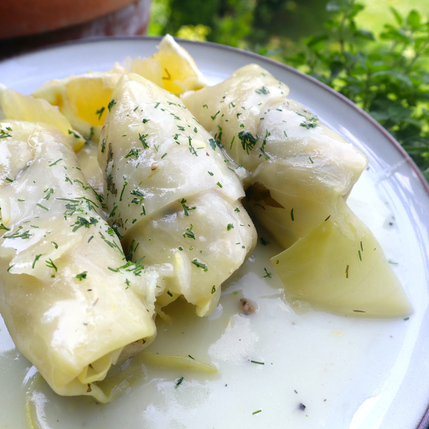 Lahanodolmades: Griechische Kohlrouladen wie bei Mama. Die Kohlrouladen: 1 Weißkohl, Salz, 500 g Rinderhackfleisch, 200 g Carolina-Reis, ½ TL Kreuzkümmel, 1 Zwiebel, 1 Knoblauchzehe, ⅓ Bund Dill, ⅓ Bund Minze, ⅓ Bund Petersilie
3 EL Rosmarin (gehackt), Pfeffer, 3–4 EL Olivenöl. Für die Sauce: 70 g Butter, 70 g Weizenmehl, 700 ml Wasser, 1 Hähnchen-Brühwürfel, Zitronenschale und -saft von 1–2 Bio-Zitronen, Pfeffer, 1 EL Olivenöl
Kohl vorbereiten:gGroßen Topf mit Salzwasser zum Kochen bringen, Strunk vom Kohls entfernen, mit der
Strunkseite nach unten ins kochende Wasser legen. Die äußeren Blätter mit einem Löffel nach und nach ablösen, sobald sie weich werden. Vorgang wiederholen, bis genug Blätter abgelöst sind. Die Blätter auf einen Gitter abkühlen lassen. Die Füllung: Hackfleisch, Reis und Kreuzkümmel in eine Schüssel geben. Zwiebel und Knoblauch fein hacken, dazugeben. Dill, Minze, Petersilie fein hacken, Stiele davon beiseitelegen. Gehackte Kräuter in die Schüssel geben. Salz, Pfeffer, Olivenöl hinzufügen, gut vermengen. In einen großen Topf die Kräuterstängel auf den Boden legen. Mit 2–3 Kohlblättern abdecken.
Die Kohlrouladen zubereiten: Von jedem Blatt die harte Mittelrippe einschneiden, entfernen. Die Enden etwas übereinnander legen, darauf 1 EL der Füllung geben. Fest einrollen, die Rouladen mit dem aufgerollten Ende nach unten dicht nebeneinander in den Topf legen, mit den restlichen Kohlblättern bedecken. Einen Teller obenauf als Gewicht legen. Mit Wasser bis zur Höhe des Tellers auffüllen, auf mittlerer Hitze ca. 1,5 Stunden köcheln lassen.
Zitronensauce: In einem Topf die Butter schmelzen, das Mehl einrühren, leicht anschwitzen. Wasser unter ständigem Rühren zugeben. Wenn die Sauce eindickt, vom Herd nehmen. Den zerdrücktren Brühwürfel, Zitronensaft, Zitronenschale, Pfeffer und Olivenöl einrühren, kurz köcheln lassen. Rouladen auf vorgewärmte Teller servieren. #griechischeKüche, #Kohlrouladen, #Lahanodolmades, #RezeptwiebeiMama, #Hausmannskost, #griechischesRezept, #Kindheitserinnerungen, #MediterraneKüche, #ComfortFood, #FoodLove, #TraditionellesEssen, #Soulfood, #GriechenlandGenuss, #EssenMitLiebe, #Rezeptideen, #foodstagram #HomemadeDelicious