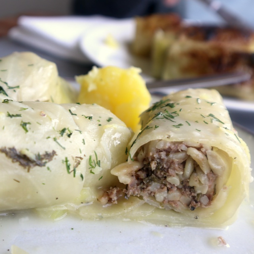 Lahanodolmades: Griechische Kohlrouladen wie bei Mama. Die Kohlrouladen: 1 Weißkohl, Salz, 500 g Rinderhackfleisch, 200 g Carolina-Reis, ½ TL Kreuzkümmel, 1 Zwiebel, 1 Knoblauchzehe, ⅓ Bund Dill, ⅓ Bund Minze, ⅓ Bund Petersilie
3 EL Rosmarin (gehackt), Pfeffer, 3–4 EL Olivenöl. Für die Sauce: 70 g Butter, 70 g Weizenmehl, 700 ml Wasser, 1 Hähnchen-Brühwürfel, Zitronenschale und -saft von 1–2 Bio-Zitronen, Pfeffer, 1 EL Olivenöl
Kohl vorbereiten:gGroßen Topf mit Salzwasser zum Kochen bringen, Strunk vom Kohls entfernen, mit der
Strunkseite nach unten ins kochende Wasser legen. Die äußeren Blätter mit einem Löffel nach und nach ablösen, sobald sie weich werden. Vorgang wiederholen, bis genug Blätter abgelöst sind. Die Blätter auf einen Gitter abkühlen lassen. Die Füllung: Hackfleisch, Reis und Kreuzkümmel in eine Schüssel geben. Zwiebel und Knoblauch fein hacken, dazugeben. Dill, Minze, Petersilie fein hacken, Stiele davon beiseitelegen. Gehackte Kräuter in die Schüssel geben. Salz, Pfeffer, Olivenöl hinzufügen, gut vermengen. In einen großen Topf die Kräuterstängel auf den Boden legen. Mit 2–3 Kohlblättern abdecken.
Die Kohlrouladen zubereiten: Von jedem Blatt die harte Mittelrippe einschneiden, entfernen. Die Enden etwas übereinnander legen, darauf 1 EL der Füllung geben. Fest einrollen, die Rouladen mit dem aufgerollten Ende nach unten dicht nebeneinander in den Topf legen, mit den restlichen Kohlblättern bedecken. Einen Teller obenauf als Gewicht legen. Mit Wasser bis zur Höhe des Tellers auffüllen, auf mittlerer Hitze ca. 1,5 Stunden köcheln lassen.
Zitronensauce: In einem Topf die Butter schmelzen, das Mehl einrühren, leicht anschwitzen. Wasser unter ständigem Rühren zugeben. Wenn die Sauce eindickt, vom Herd nehmen. Den zerdrücktren Brühwürfel, Zitronensaft, Zitronenschale, Pfeffer und Olivenöl einrühren, kurz köcheln lassen. Rouladen auf vorgewärmte Teller servieren. #griechischeKüche, #Kohlrouladen, #Lahanodolmades, #RezeptwiebeiMama, #Hausmannskost, #griechischesRezept, #Kindheitserinnerungen, #MediterraneKüche, #ComfortFood, #FoodLove, #TraditionellesEssen, #Soulfood, #GriechenlandGenuss, #EssenMitLiebe, #Rezeptideen, #foodstagram #HomemadeDelicious